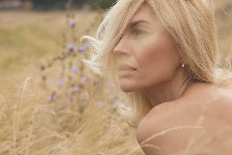 Close-up portrait of a blonde woman in summer field with pensive expression.