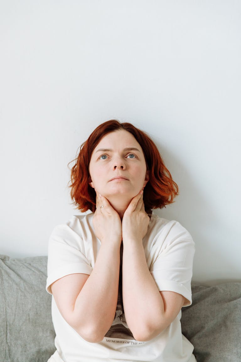 Contemplative woman with red hair touching her neck, exuding introspection in a calm environment.