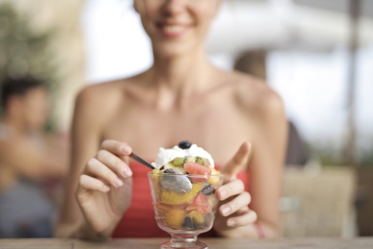 Happy woman eating fruit salad at a cafe, enjoying a refreshing dessert.