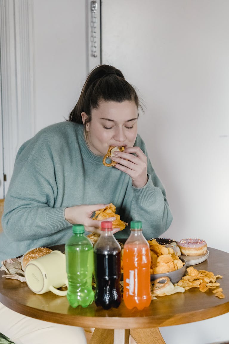 Young woman enjoys assorted fast food and snacks indoors with a variety of sodas.